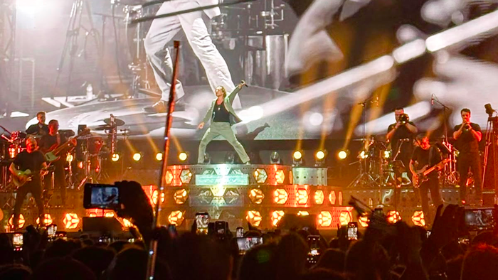 David Bisbal singing on stage at Cooltural Fest, Almería, with the band and lighting rig behind him and the crowd filming on phones in front.