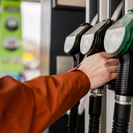 A person's hand holding a fuel pump nozzle at a petrol station forecourt.
