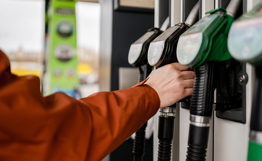 A person's hand holding a fuel pump nozzle at a petrol station forecourt.