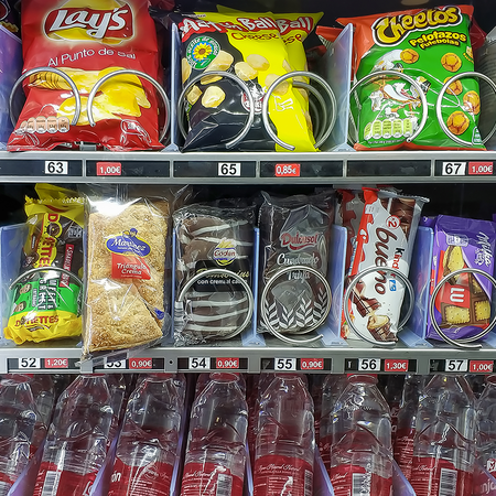 A hospital vending machine stocked with crisps, chocolate bars and biscuits on the top two rows and bottled water on the bottom row.
