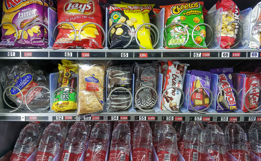 A hospital vending machine stocked with crisps, chocolate bars and biscuits on the top two rows and bottled water on the bottom row.