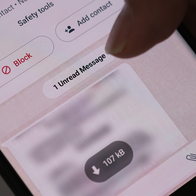 Close-up of a hand holding a smartphone showing a WhatsApp chat with a Block option and an unread message.