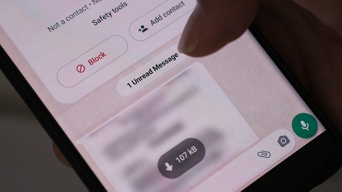 Close-up of a hand holding a smartphone showing a WhatsApp chat with a Block option and an unread message.