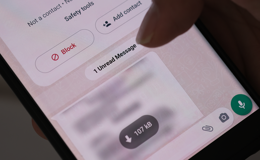 Close-up of a hand holding a smartphone showing a WhatsApp chat with a Block option and an unread message.