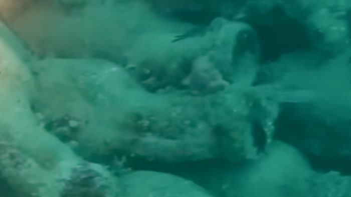 Encrusted clay amphorae scattered across the seabed in blue water.