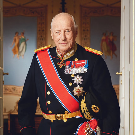King Harald V of Norway standing in official military dress uniform with medals and sash, in a palace doorway.