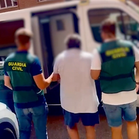 Two Guardia Civil officers escorting a blurred male suspect towards a police vehicle.