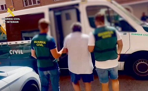 Two Guardia Civil officers escorting a blurred male suspect towards a police vehicle.