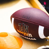 An American football placed on a training bech next to an orange training cone