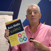 Michael O'Leary holding a book called "Math for Dummies" in front of a Ryanair branded wall during his speech in a recent YouTube video.
