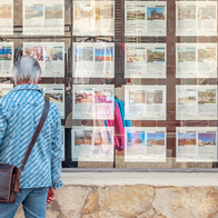 Person looking at rows of property listings displayed in a Spanish estate-agent window.