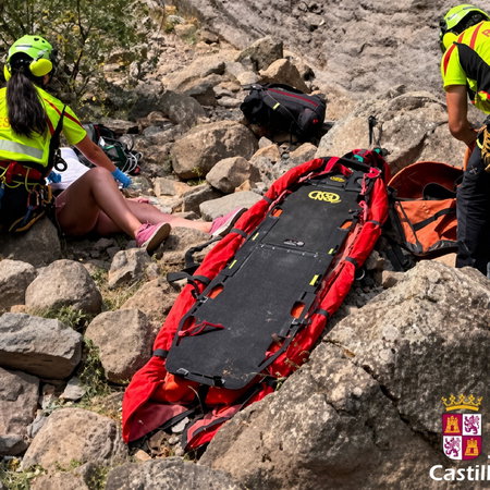 Mountain rescue team assisting an injured person on rocky terrain with a red stretcher.