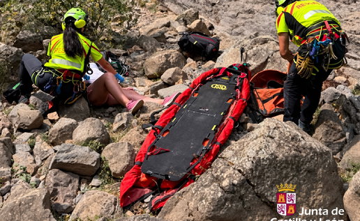 Mountain rescue team assisting an injured person on rocky terrain with a red stretcher.