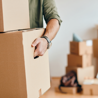 A man carries cardboard moving boxes inside an apartment.