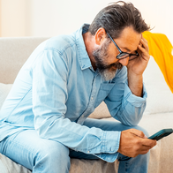 Person holding their head in their hand as they look worried at their phone.