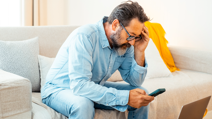 Person holding their head in their hand as they look worried at their phone.