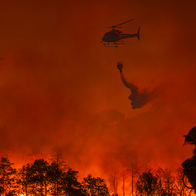 Two firefighting helicopters amongst the smoke and ashes trying to extinguish a wildfire