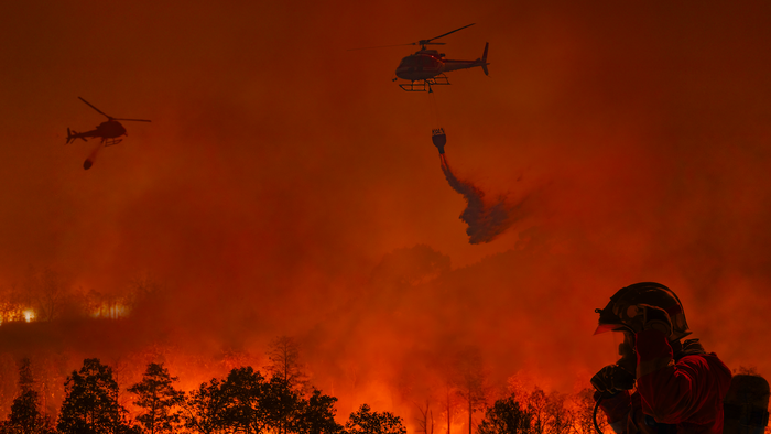 Two firefighting helicopters amongst the smoke and ashes trying to extinguish a wildfire