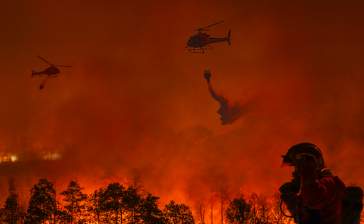 Two firefighting helicopters amongst the smoke and ashes trying to extinguish a wildfire