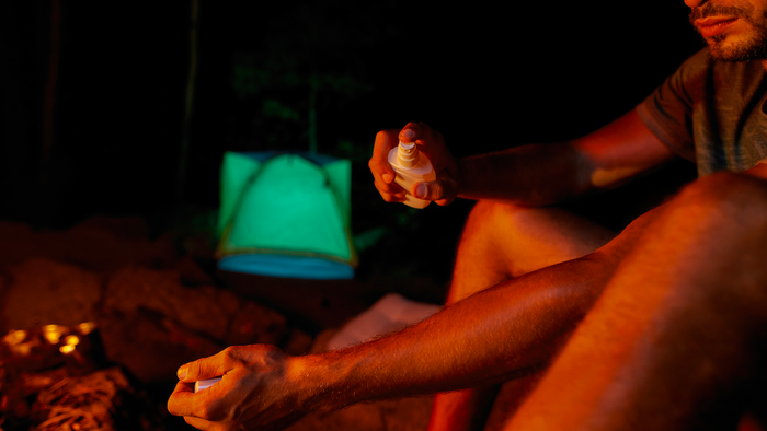 Man applying mosquito repellent next to a camp fire