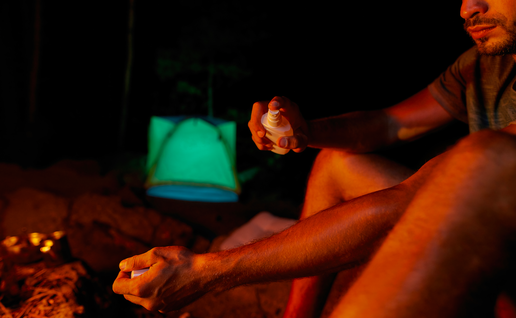 Man applying mosquito repellent next to a camp fire