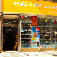 An exterior view of a supermarket in Malaga, Spain with a woman walking past it.