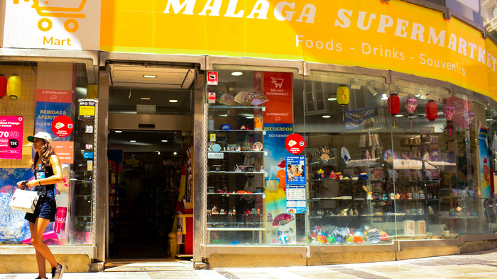 An exterior view of a supermarket in Malaga, Spain with a woman walking past it.