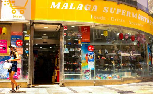 An exterior view of a supermarket in Malaga, Spain with a woman walking past it.
