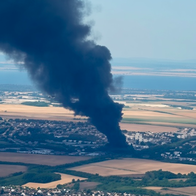 Aerial view of a town with a large thick black smoke plume rising into the sky over fields and houses.