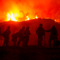 The silhouette of firefighters with the flames of a wildfire behind them