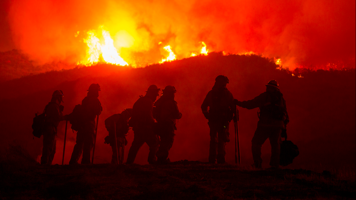 The silhouette of firefighters with the flames of a wildfire behind them