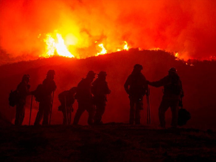 The silhouette of firefighters with the flames of a wildfire behind them