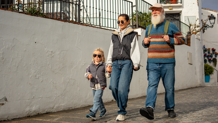 An elder man walking with his daughter and grandson down a street