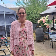 A woman in a pink dress in a back garden with balloons and parasols