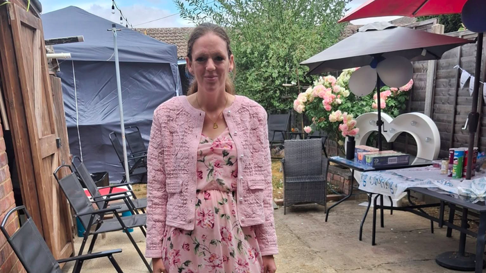 A woman in a pink dress in a back garden with balloons and parasols