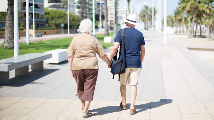 Elderly couple holding hands as they walk down a Spanish seafront.