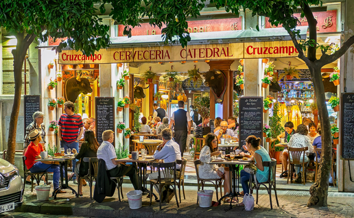 People sat at tables on a pavement outside a traditional Spanish bar.