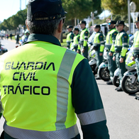A Guardia Civil Tráfico officer in a hi-vis jacket faces rows of fellow officers and motorcycles lined up on a street.