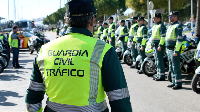 A Guardia Civil Tráfico officer in a hi-vis jacket faces rows of fellow officers and motorcycles lined up on a street.