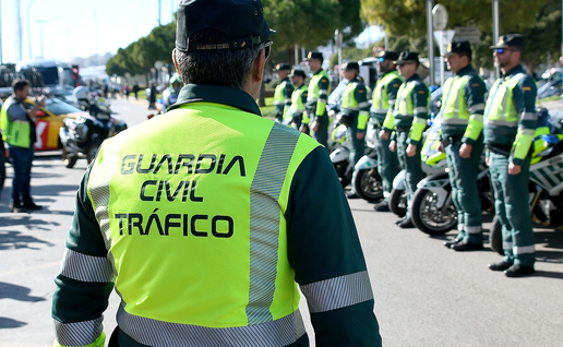A Guardia Civil Tráfico officer in a hi-vis jacket faces rows of fellow officers and motorcycles lined up on a street.