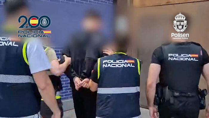 Spanish national police walk the Swedish fugitive into custody.