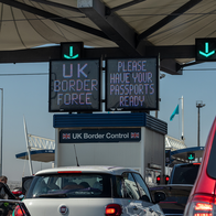 Vehicles waiting beneath UK Border Force signs at a border checkpoint.