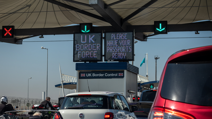 Vehicles waiting beneath UK Border Force signs at a border checkpoint.