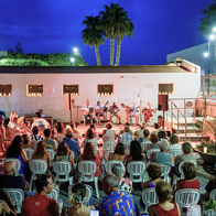 Audience gathers between candlelit walls in front of a stage of musicians performing at Vera's Plaza de los Cuatro Caños.