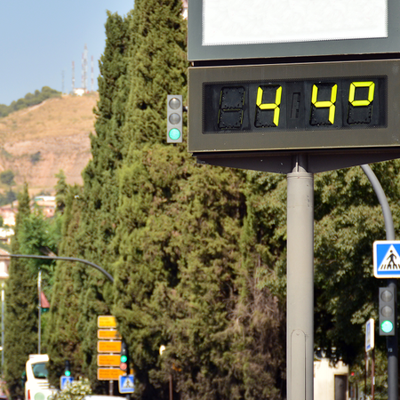 A digital street thermometer in a Spanish city displaying 44 degrees Celsius on a sunny day, with traffic and trees in the background.
