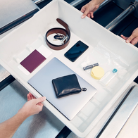 Personal items inside a plastic tray on a security conveyor at an airport.