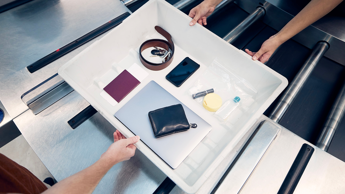 Personal items inside a plastic tray on a security conveyor at an airport.