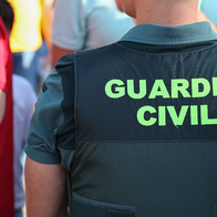 Close-up of the back of a Guardia Civil vest reading 'Guardia Civil' in green lettering, photographed in a crowd.