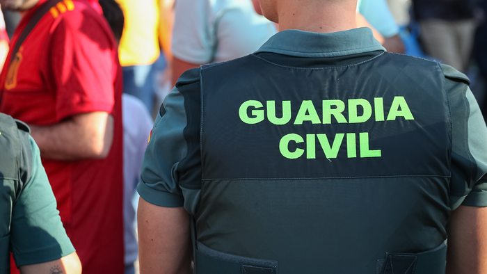Close-up of the back of a Guardia Civil vest reading 'Guardia Civil' in green lettering, photographed in a crowd.