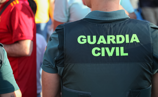 Close-up of the back of a Guardia Civil vest reading 'Guardia Civil' in green lettering, photographed in a crowd.